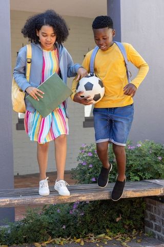 School children stepping off bench holding soccer ball and folder after school