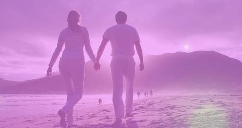 Walking couple holding hands on sunset beach with wet sand reflections and footprints