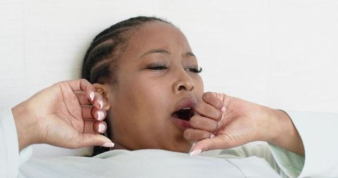 Yawning african american woman reclining on bed in light robe with nose ring and manicure