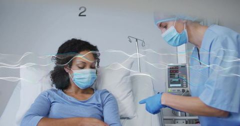 Nurse pointing at infusion pump explaining treatment to masked patient in hospital bed
