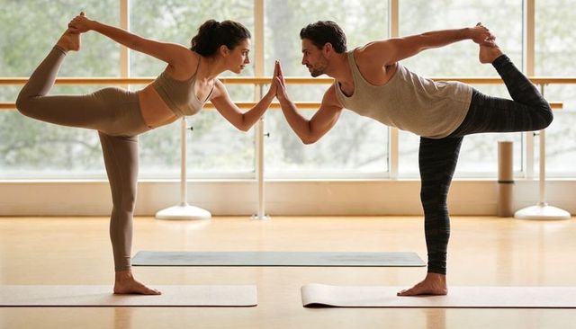 Couple practicing partner yoga in bright studio holding dancer pose and balancing