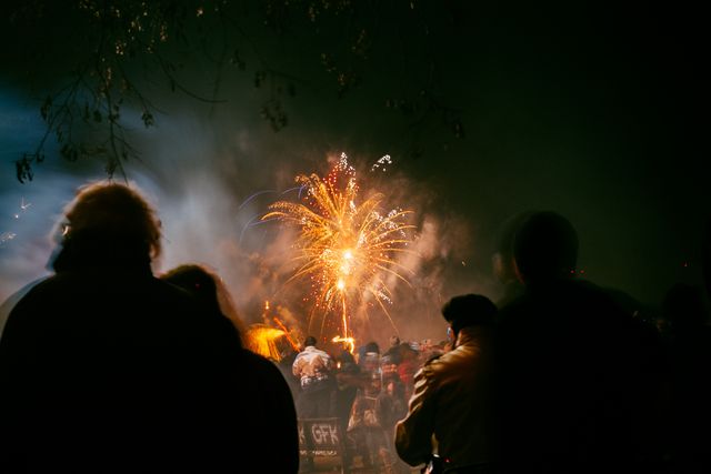 People gathering on a street against colorful fireworks exploding in the night sky. New years eve and celebration concept