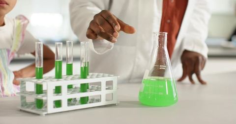 African Scientist Teaching Children Chemistry with Bright Green Solution in Lab Classroom