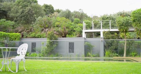 Ornate White Metal Garden Chair and Round Table on Lush Lawn by Glass Pool Fence