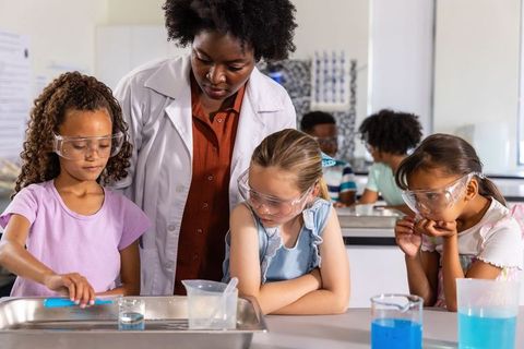 Teacher guiding school girls conducting classroom science experiment with pipette