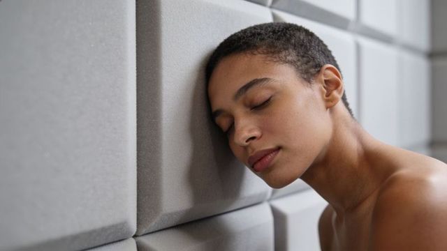 Short-haired woman resting head on gray acoustic foam panels, minimalist calm portrait