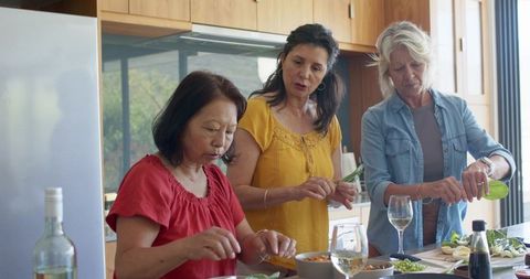 Diverse women cooking together in sunlit modern kitchen sharing fresh meal and wine