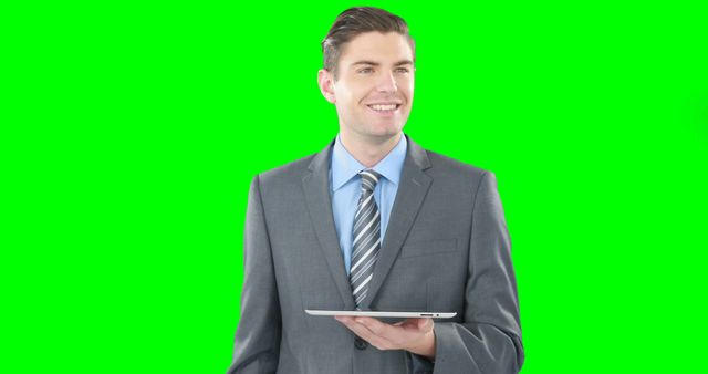 Businessman wearing suit and tie holding tablet with green screen background. Ideal for presentations, corporate videos, technology showcases, or business marketing materials. Can be used to insert custom backgrounds or digital content.