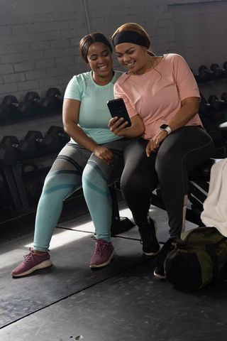 African american friends checking workout progress on smartphone while resting on gym bench