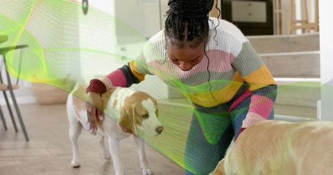 Kneeling woman bonding with two dogs in bright home interior wearing striped sweater