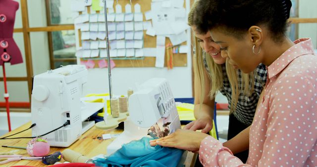 Diverse female fashion designers talking at sewing machine in fashion design studio, copy space. Teamwork, fashion, clothing, sewing and creative business, unaltered.
