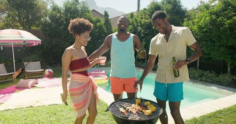 Friends Enjoy Grilling Kebabs and Corn Poolside in Lively Backyard