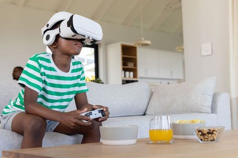 Preteen african american boy wearing vr headset playing games on couch in living room