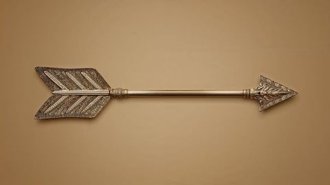Ornate metal arrow with intricate engravings on tan backdrop