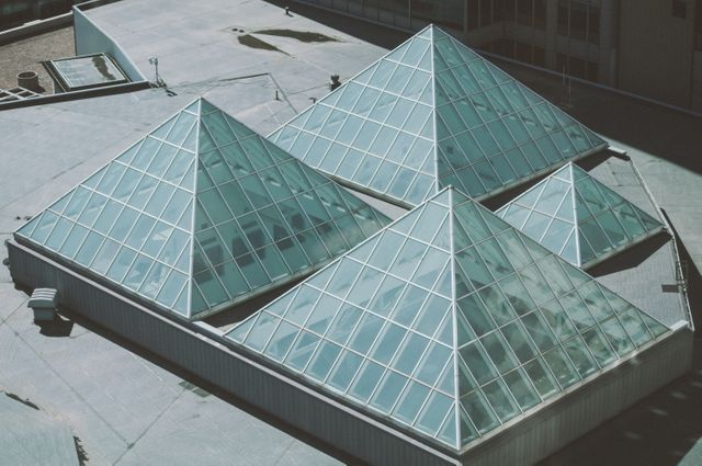 This image showcases a set of modern glass pyramid skylights on top of a building roof. The geometric design and transparent material add a contemporary touch to the urban architectural landscape. This photo can be used for topics related to modern architecture, urban environments, geometric designs, or innovative building constructions.