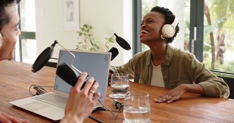 Diverse coworkers recording podcast, laughing together around laptop with studio microphones