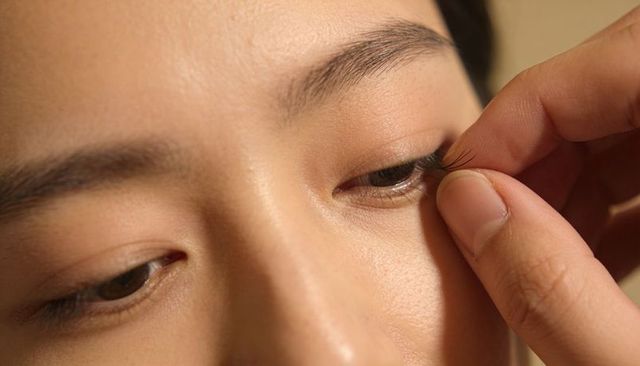 Applying false eyelashes on asian woman using fingertips close-up beauty makeup detail