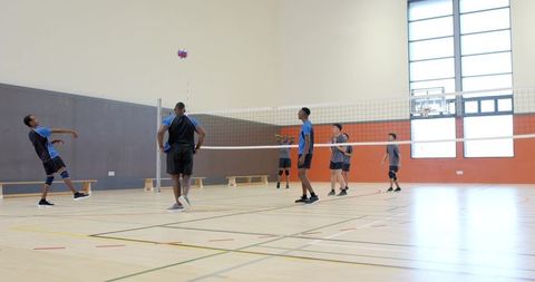 Male volleyball players practicing indoor school gym team playing colorful ball and net