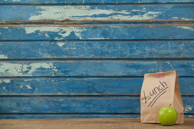 Apple and lunch bag against blue wooden background