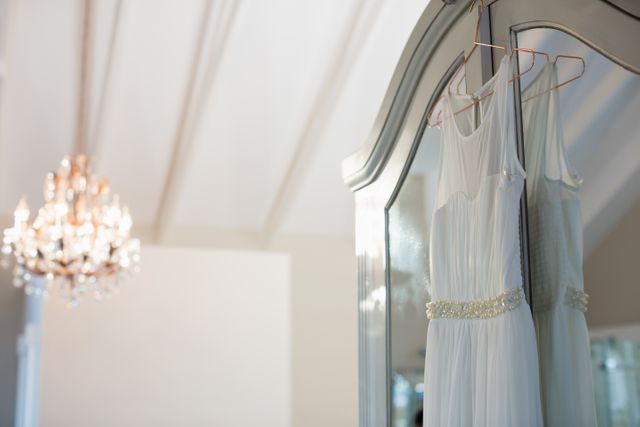 Elegant wedding dress hanging on a mirror in a home setting, with a chandelier in the background. Ideal for use in wedding planning materials, bridal fashion promotions, and interior design inspiration.
