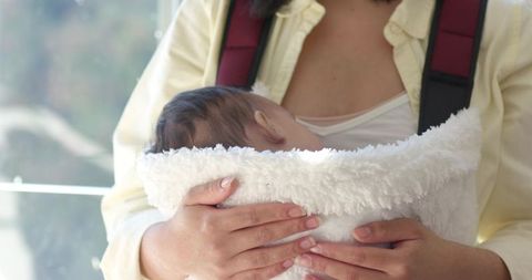 Mother holding baby in carrier by sunlit window