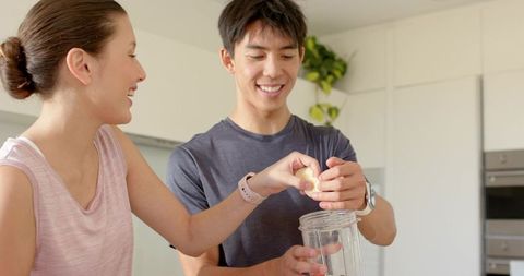 Young couple preparing smoothie together in bright modern kitchen, smiling