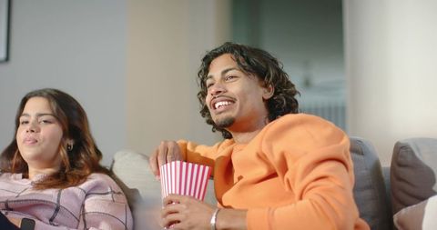 Couple enjoying cozy movie night on sofa with popcorn and casual knitwear