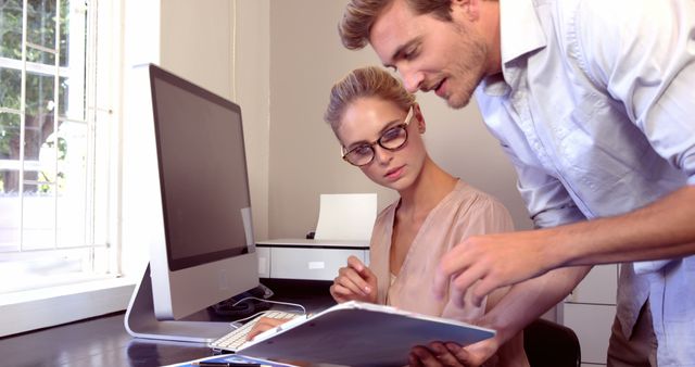 Serious woman working on computer while man showing a file in the office at home - Download Free Stock Photos Pikwizard.com