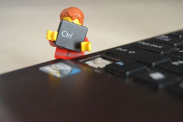 Lego figure holding large computer key standing next to keyboard with missing key. Great for concepts illustrating problems with technology, innovation, or playful solutions. Ideal for blogs, educational materials, social media posts about tech issues, creativity, or problem-solving in a fun, engaging way.