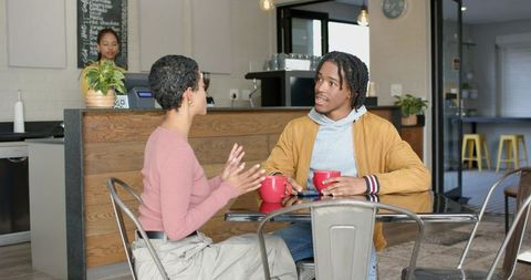 Sharing conversation over coffee in modern cafe with red mugs and warm wood counter