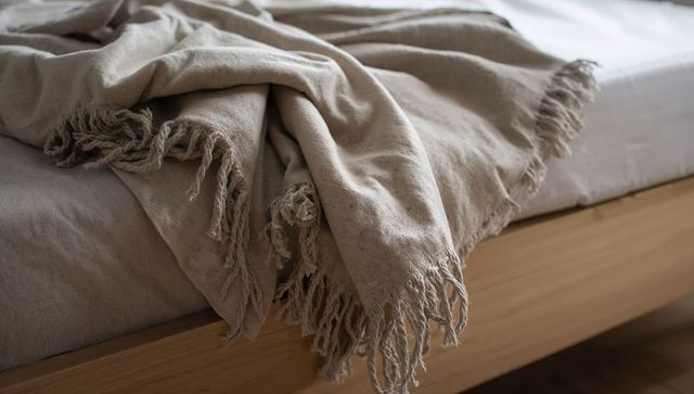 Draping beige fringed throw over wood platform bed with soft sunlight and natural texture
