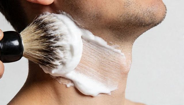 Shaving brush applying rich lather to male jawline and neck closeup for grooming routine