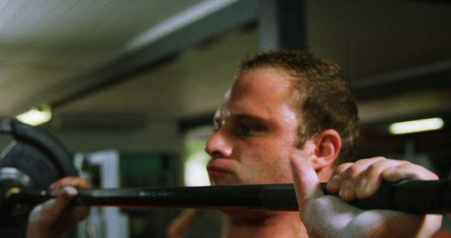 Man engaging in weightlifting exercise in indoor gym. Suitable for illustrating fitness-related content, promoting gym memberships, or representing dedication to physical health.