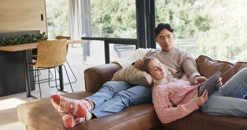 Sunlit couple relaxing on leather sofa using tablet in modern living room