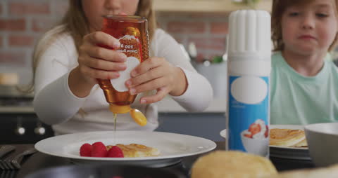 Child Pouring Honey on Pancake with Berries and Cream