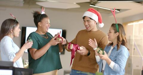 Multicultural team exchanging wrapped gifts and celebrating holiday spirit in modern office