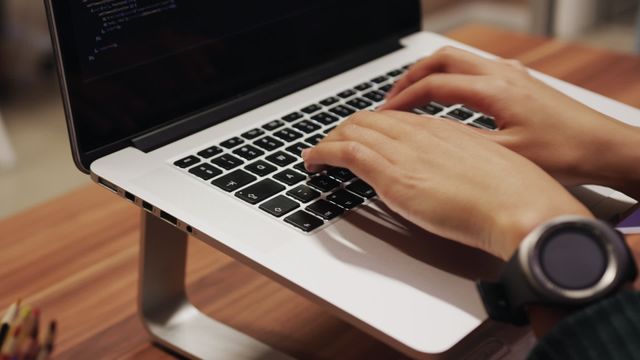 Close up detail of a mixed race businesswoman working in a modern office, typing fast on a laptop computer on desk stand