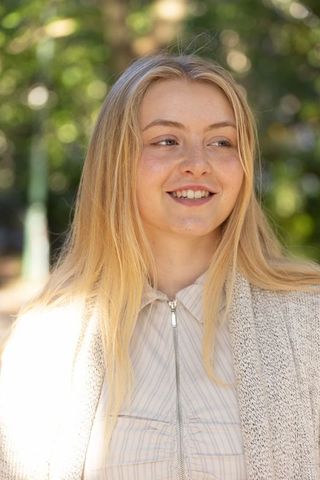 Smiling young woman enjoying sunlight in park wearing knit cardigan and zip-front top