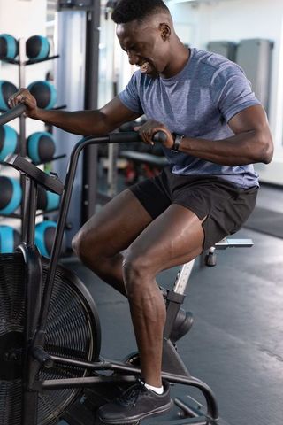 African american athlete pushing hard on air bike for intense cardio training gym session