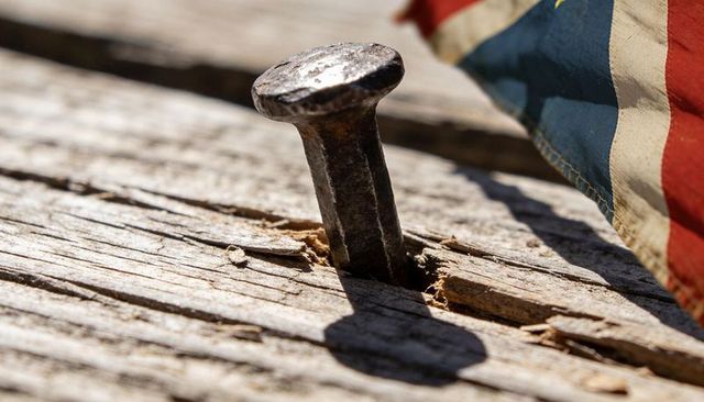Rusting square-headed nail in weathered wood with american flag fragment, macro texture