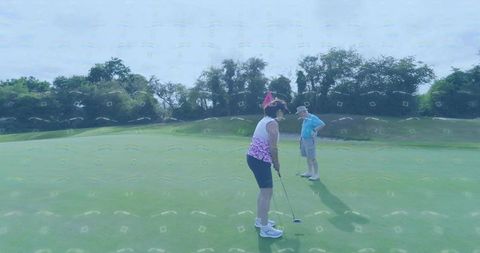 Mature woman putting on golf green while partner watching near flagstick, senior couple