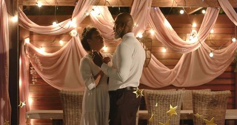Romantic evening dance under pink drapery and string lights at wooden pavilion
