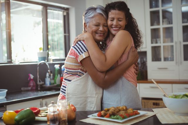 Mother and daughter embracing in a cozy kitchen, surrounded by fresh vegetables and prepared food. Ideal for themes of family love, bonding, and domestic life. Perfect for use in advertisements, blogs, and articles about family relationships, home cooking, and multigenerational living.