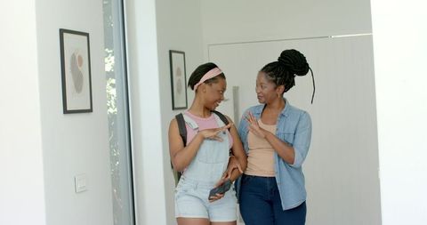 African mother and teenage daughter walking arm-in-arm in bright modern foyer wearing denim