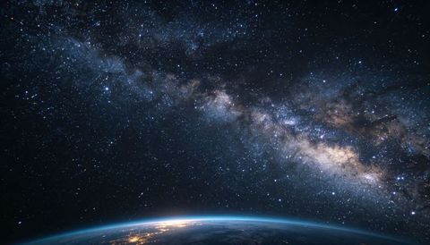 Milky way arcing over low earth horizon showing limb glow, city lights, galactic core and starfield