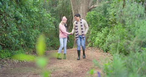 Couple walking hand in hand on woodland trail wearing rubber boots and striped scarf