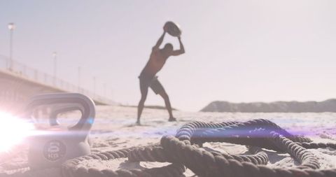 African American Man Exercising on Sunny Beach with Kettlebell