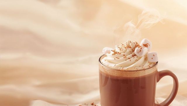 Steaming hot cocoa with whipped cream and marshmallows in brown mug on beige background