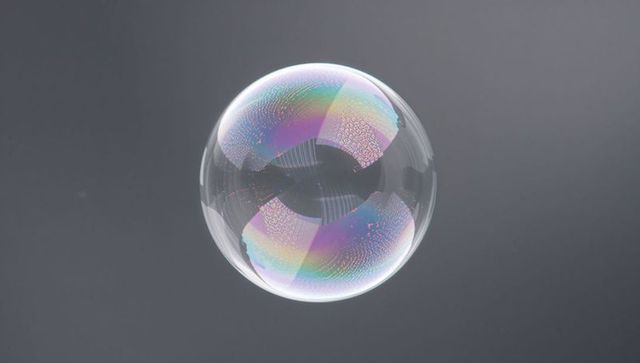 Floating iridescent soap bubble showing rainbow thin-film patterns on grey backdrop