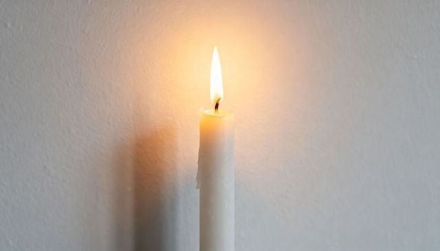 Burning White Taper Candle with Warm Glow Casting Long Soft Shadow on Painted Wall